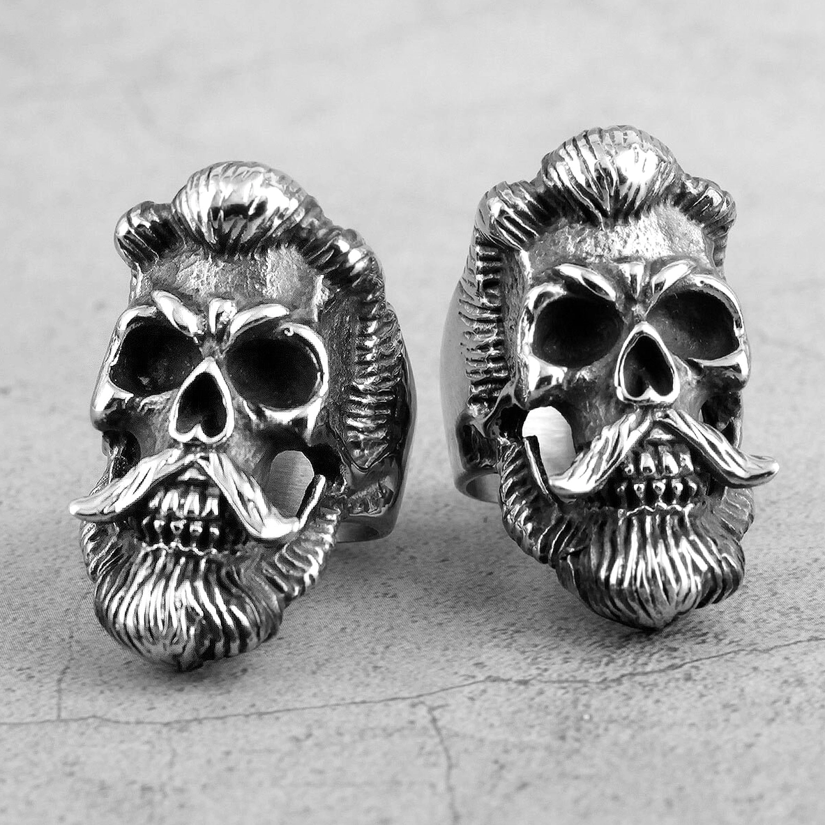 Two bearded skull gothic rings placed on grey concrete textured background statement piece