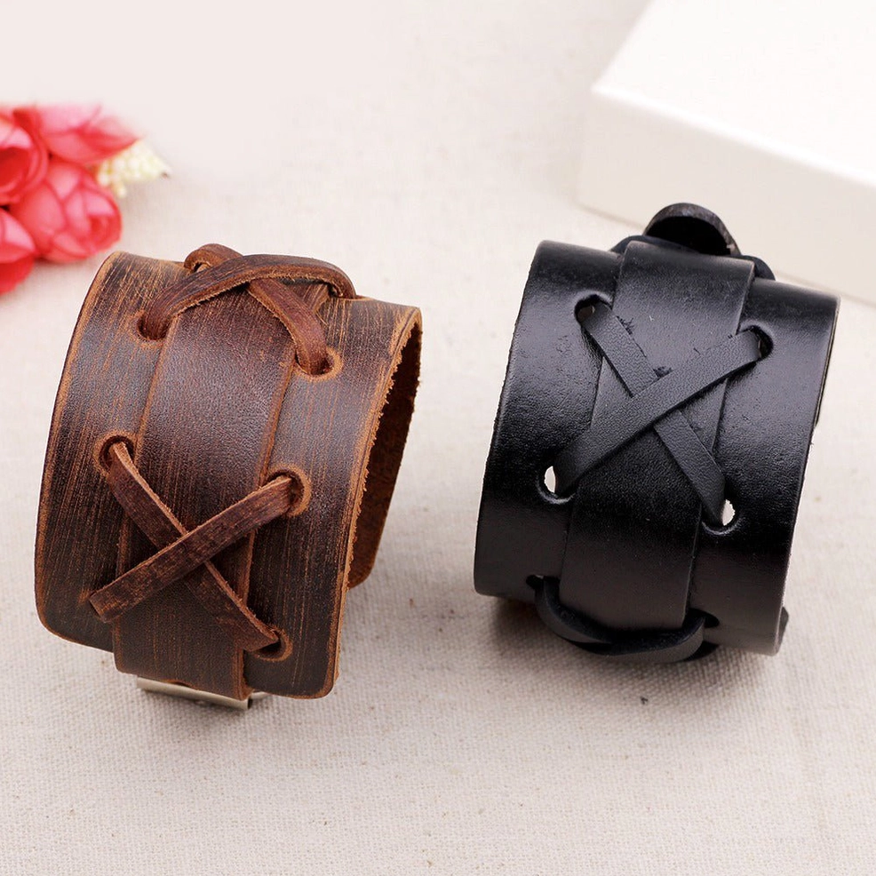 Flat lay comparison of black and brown genuine leather gothic cross-lace wristbands displayed together with decorative styling elements