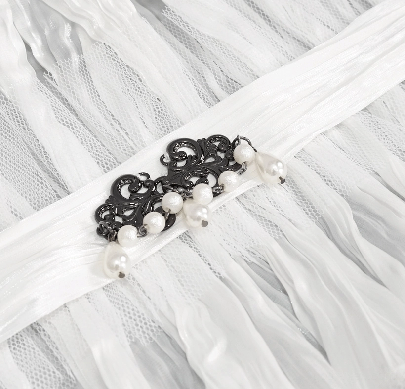Extreme close-up of ornate black metal brooch with dangling pearl embellishments on white gothic collar
