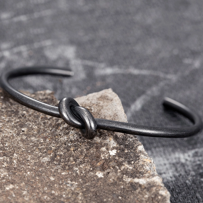 Overhead flat lay of black oxidized stainless steel knotted bracelet on textured stone background