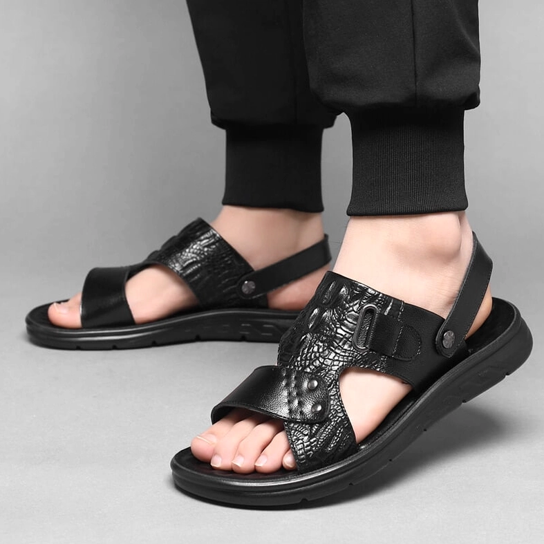 Black crocodile leather sandals worn on male model with cropped black pants, front low angle showcasing on-foot styling
