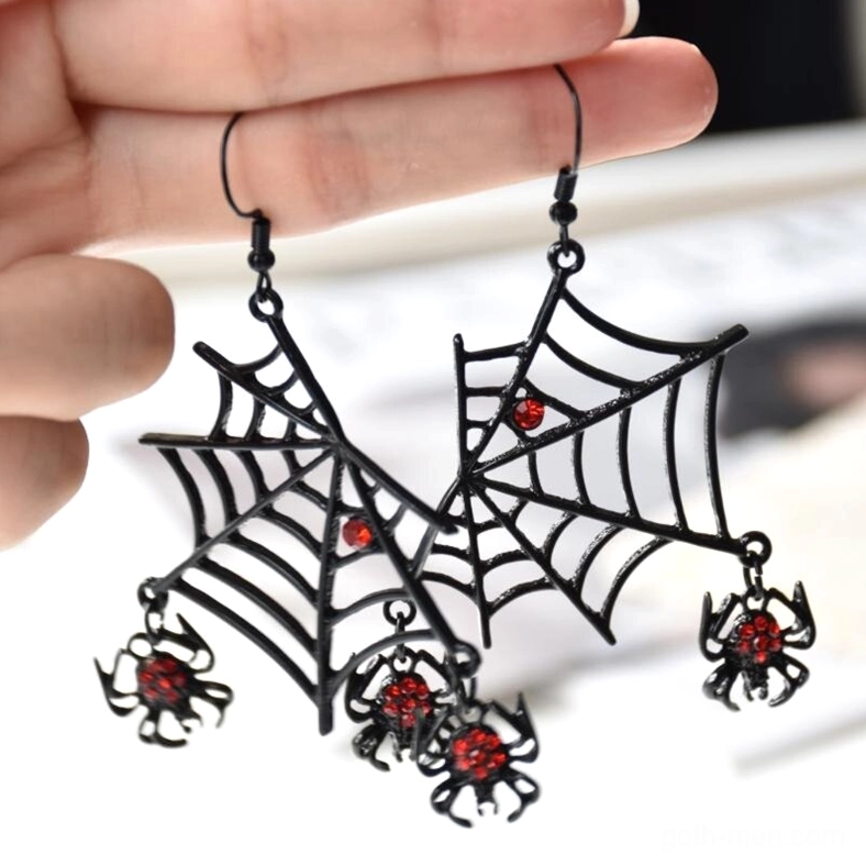 Hand holding black spider earrings with red rhinestone accents, close-up front view showcasing web and spider charm details