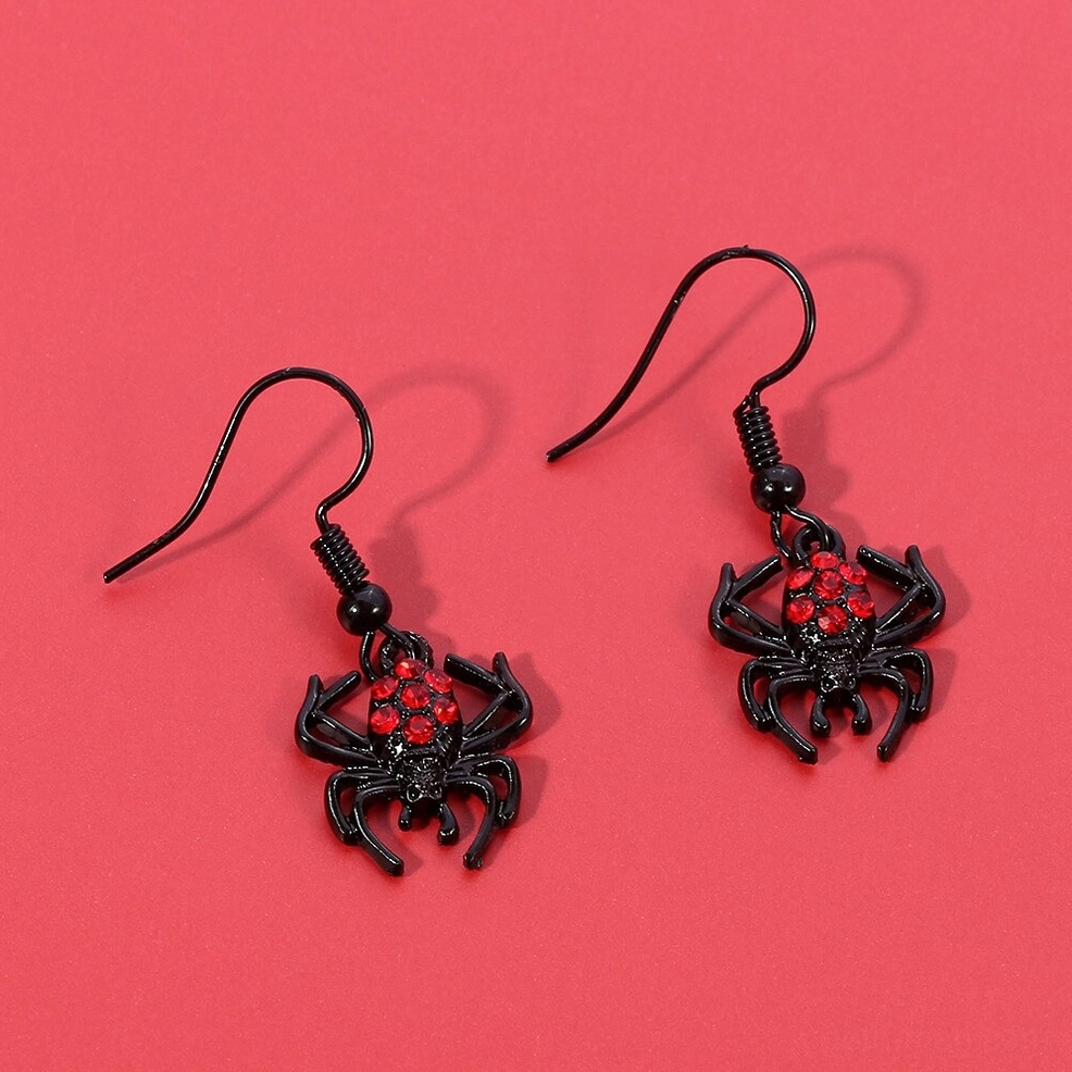 Black metal spider earrings with red crystal details, top-down flat lay on red background with soft shadows, alternative fashion jewelry