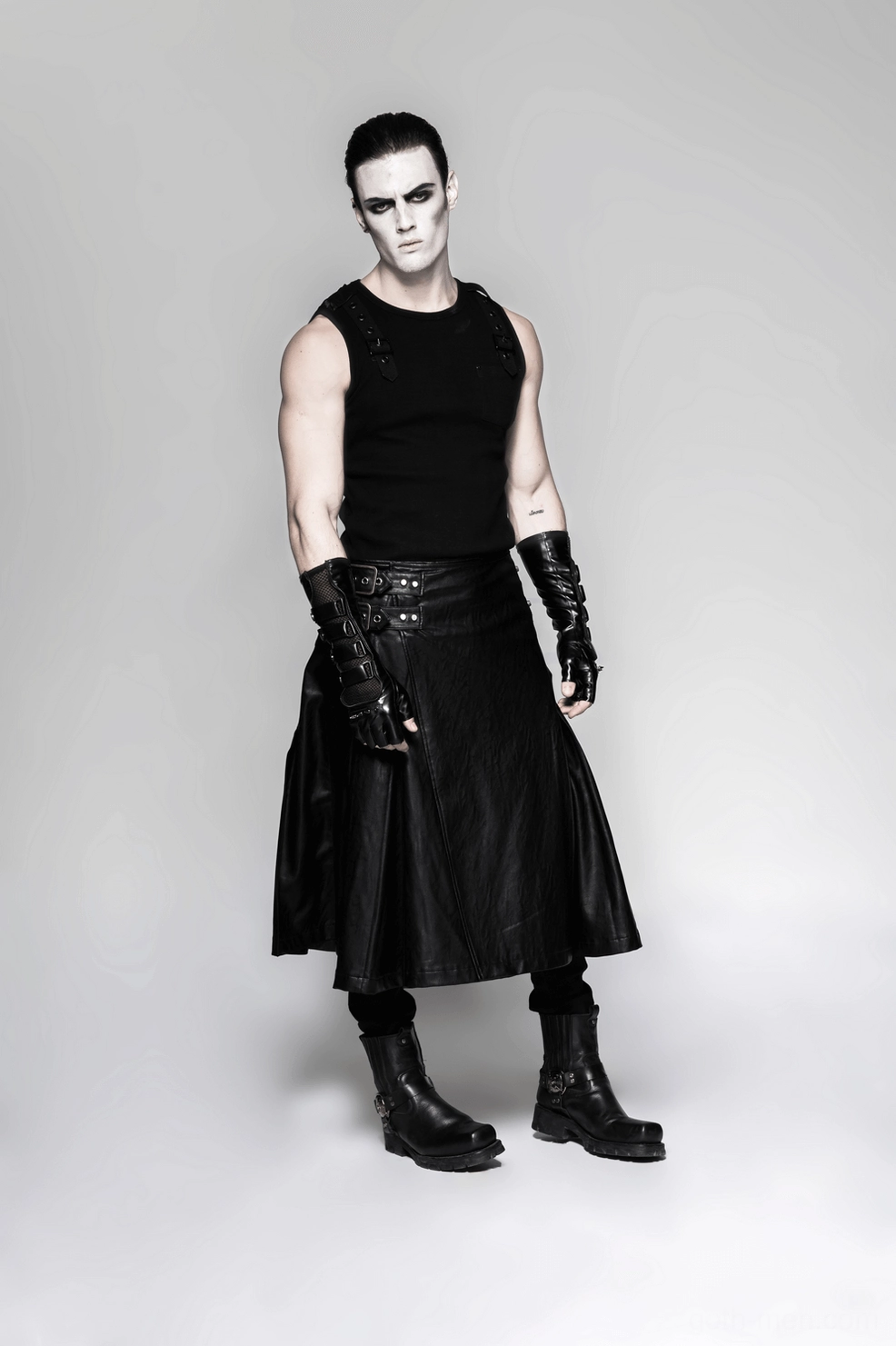 Full front body view of male model wearing black gothic ensemble with spiked gauntlet gloves and leather skirt