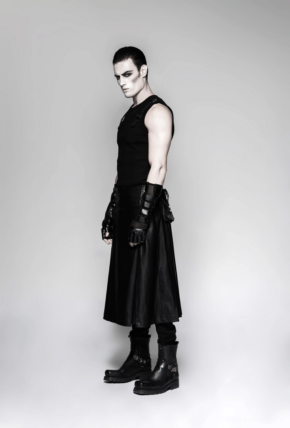 Side view of male model in gothic outfit with black spiked gauntlet gloves, leather skirt, and combat boots