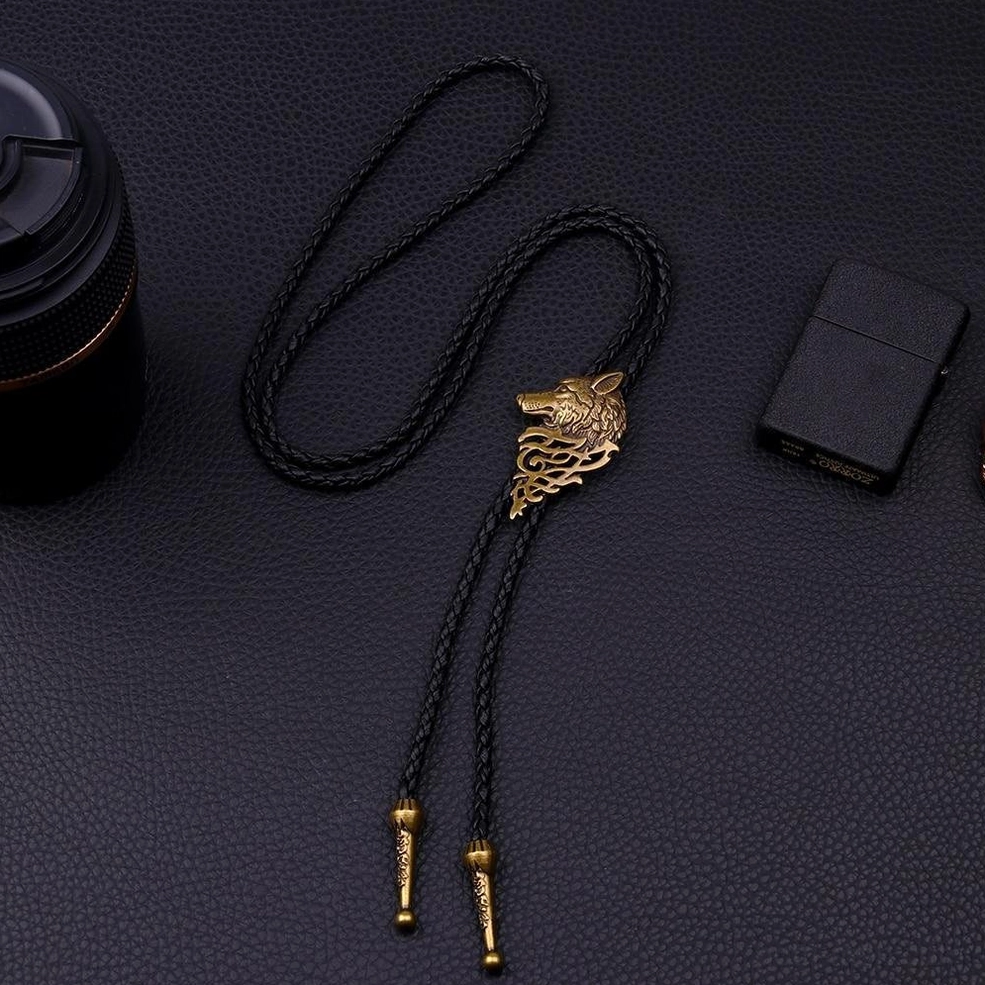 Bronze wolf head bolo tie necklace top-down view on dark leather, alternative fashion gothic pendant with styling props