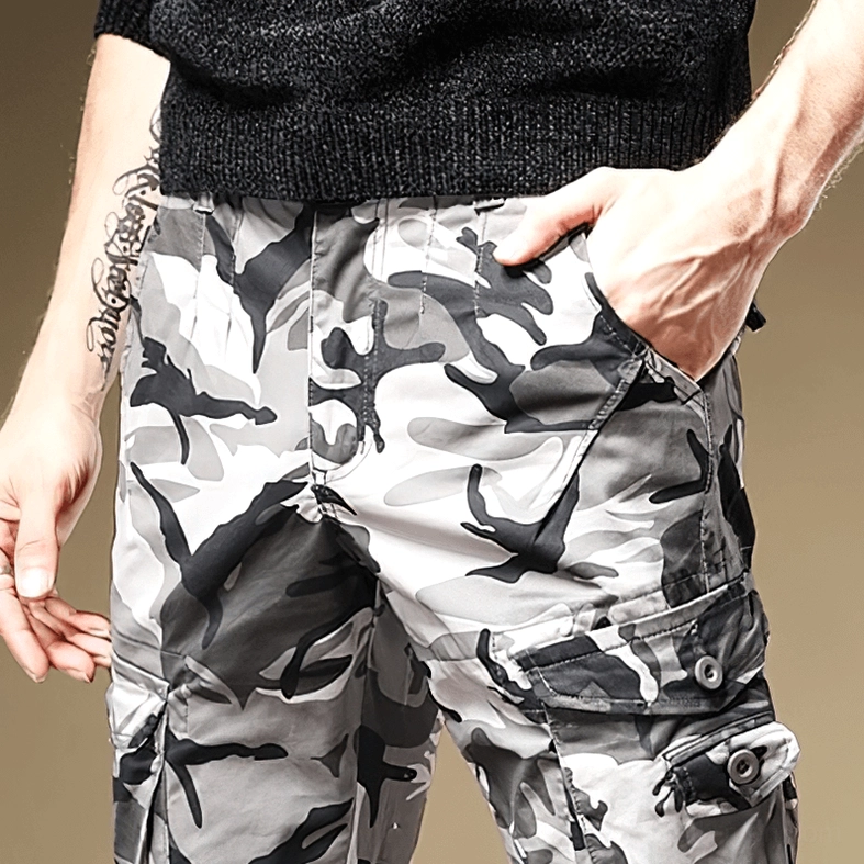 Close-up detail of buttoned side cargo pocket on light gray camouflage pants with hand demonstration
