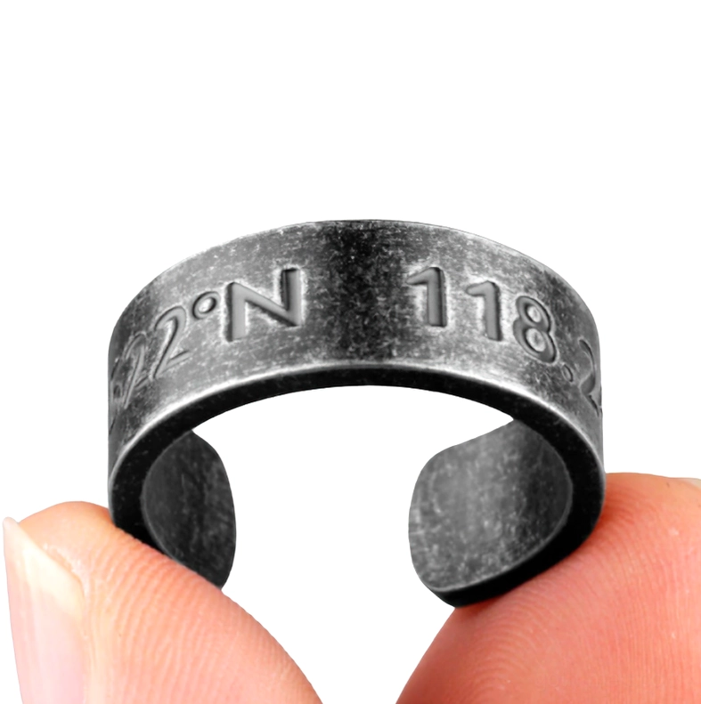 Open cuff coordinate ring worn on finger, close-up showing partial coordinate engraving and dark metal texture
