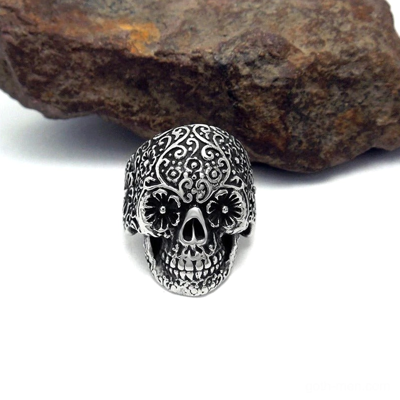 Dark silver gothic skull ring on stone surface, intricate carved floral patterns, punk rock alternative jewelry