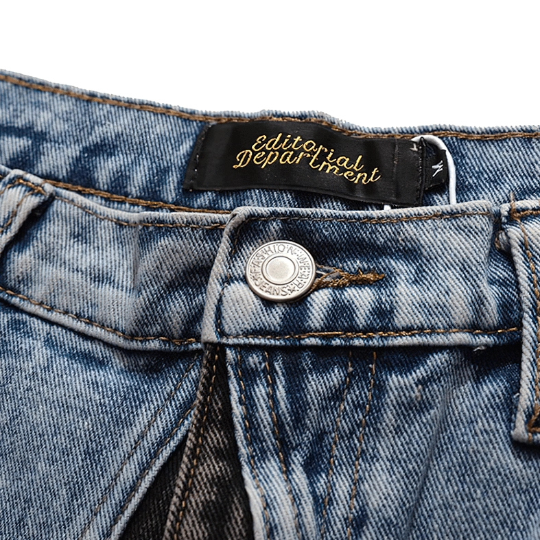 Close-up of waistband detail on gothic denim shorts showing button fly closure, branded woven tag, and yellow contrast stitching
