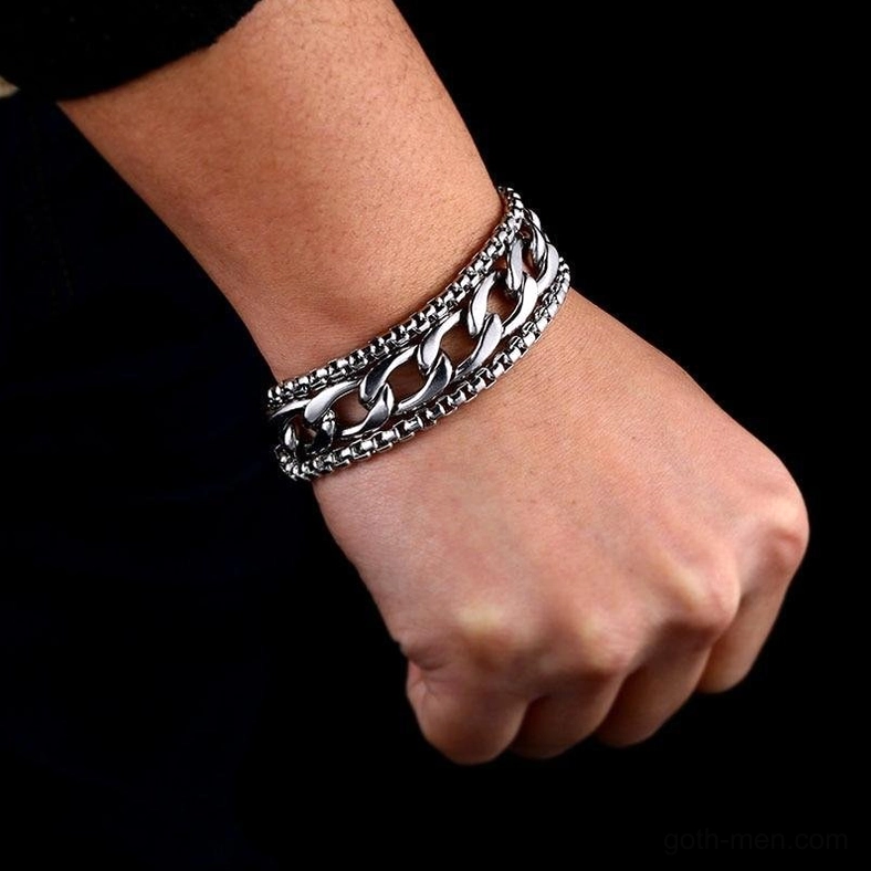 Double-chain stainless steel bracelet on clenched male fist side close-up pure black background, tough punk silver polished gothic jewelry
