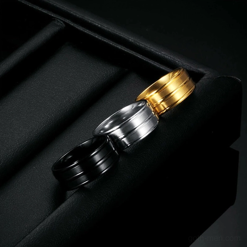 Stainless steel gothic band rings arranged in black leather tray slots, overhead product photography