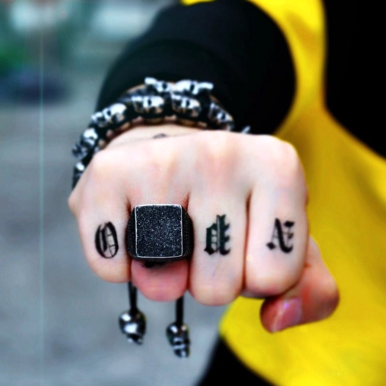 Aged black stainless steel gothic square ring on tattooed hand with beaded bracelet outdoor