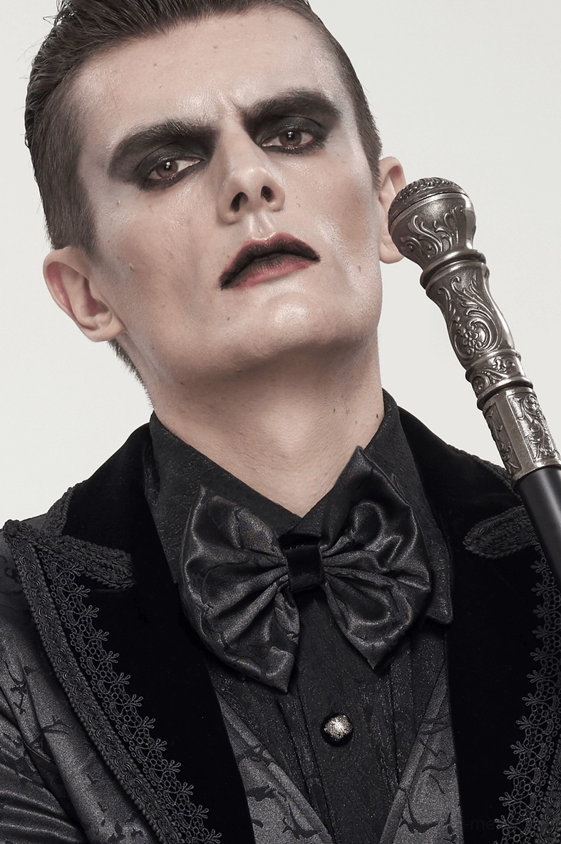 Male model wearing black gothic bow tie with walking cane and velvet-trimmed goth suit three-quarter portrait