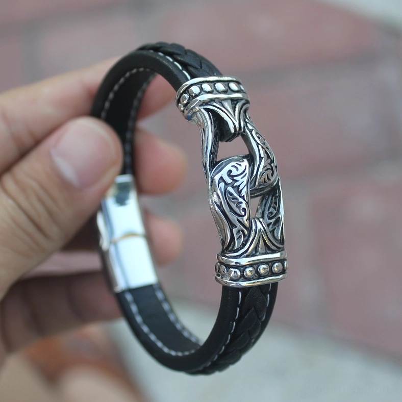 Hands holding gothic leather bracelet showing carved metal buckle and magnetic clasp design detail