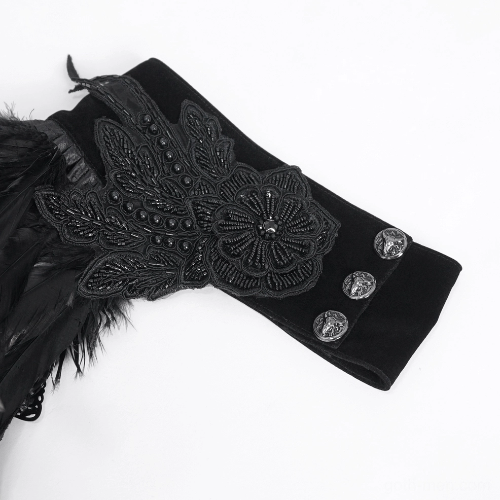 Close-up flat lay of gothic cape collar detail showing black feathers, beaded floral embroidery, and ornate metal decorative buttons