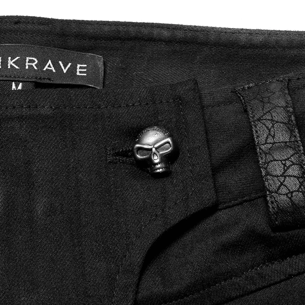 Hardware close-up of black gothic cargo pants featuring skull-shaped metal waist button and brand label detail