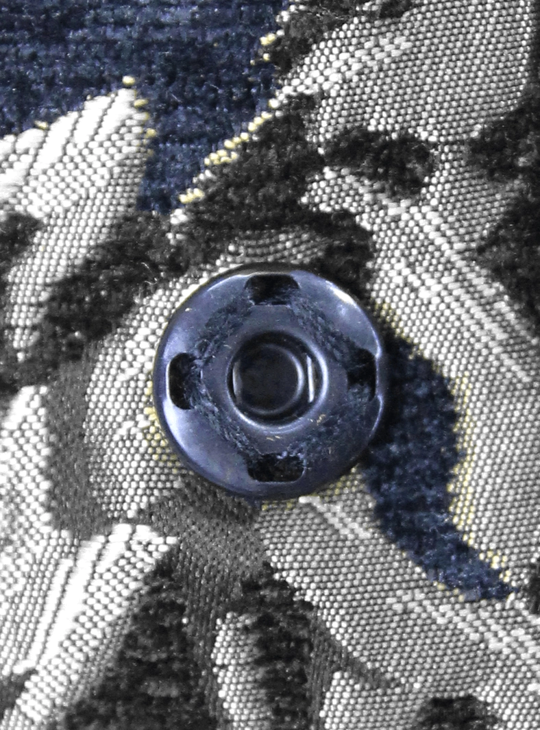 Round dark metal button mounted on silver damask jacquard gothic coat textile close-up