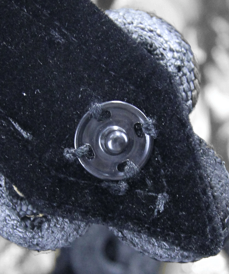Black velvet fabric with stitched metal button mounting detail on gothic sleeveless coat