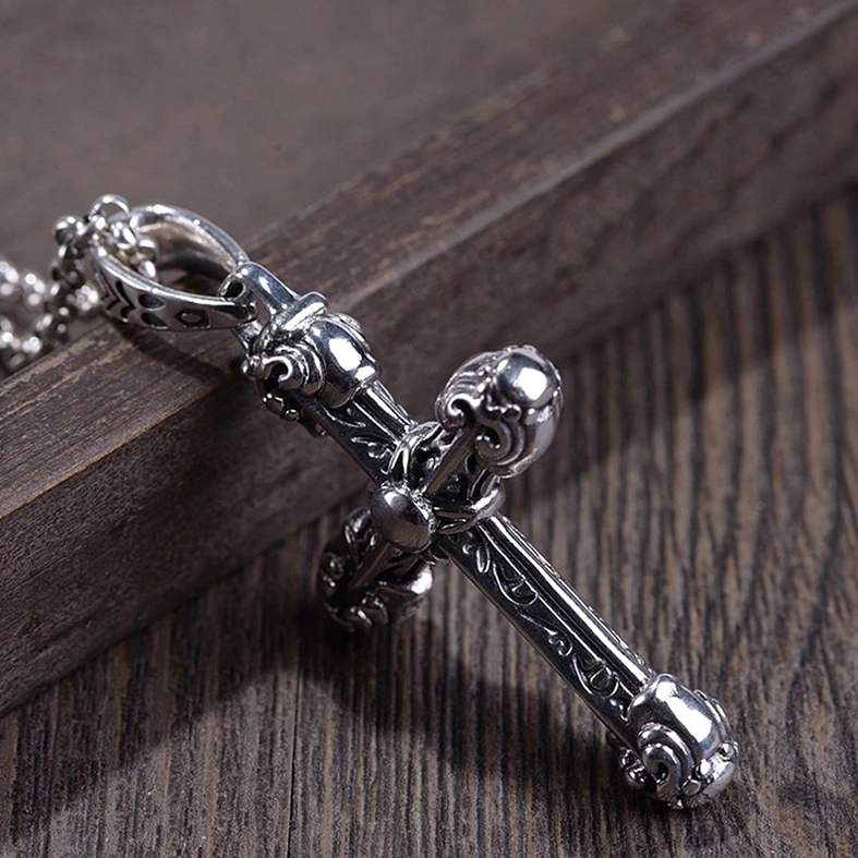 vintage-style gothic cross pendant featuring polished silver metal with scroll carvings and rounded cross end caps, side view