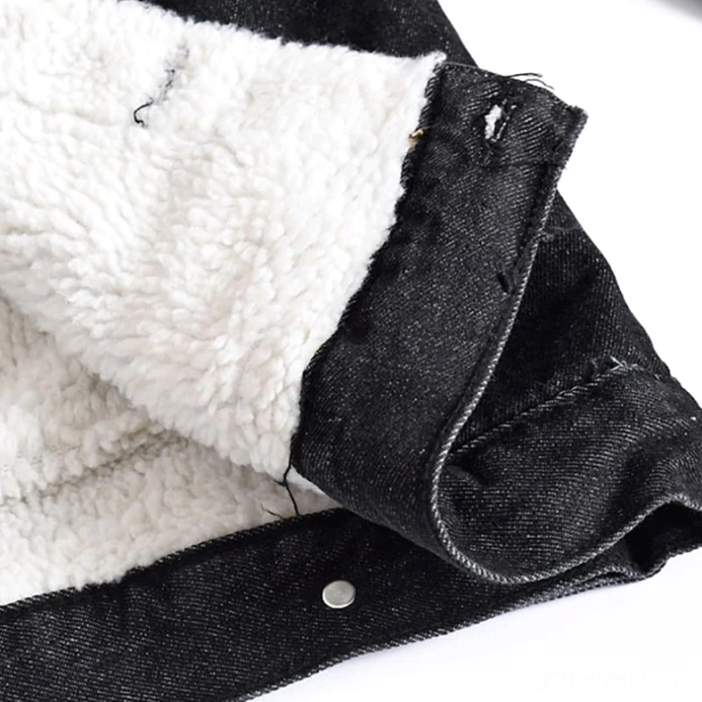 Black denim jacket inner sherpa fleece lining close-up showing thick white thermal layer and metal snap fastener, gothic craftsmanship