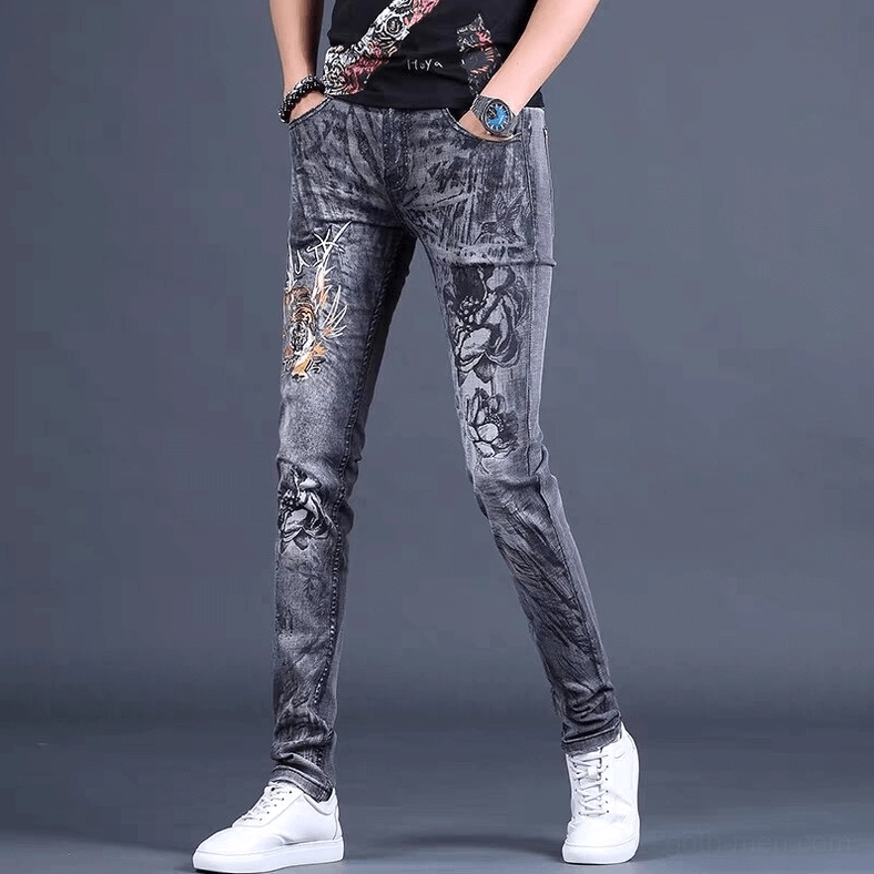 Three-quarter front angle of gothic dragon embroidered skinny jeans in grey denim with hands in pockets