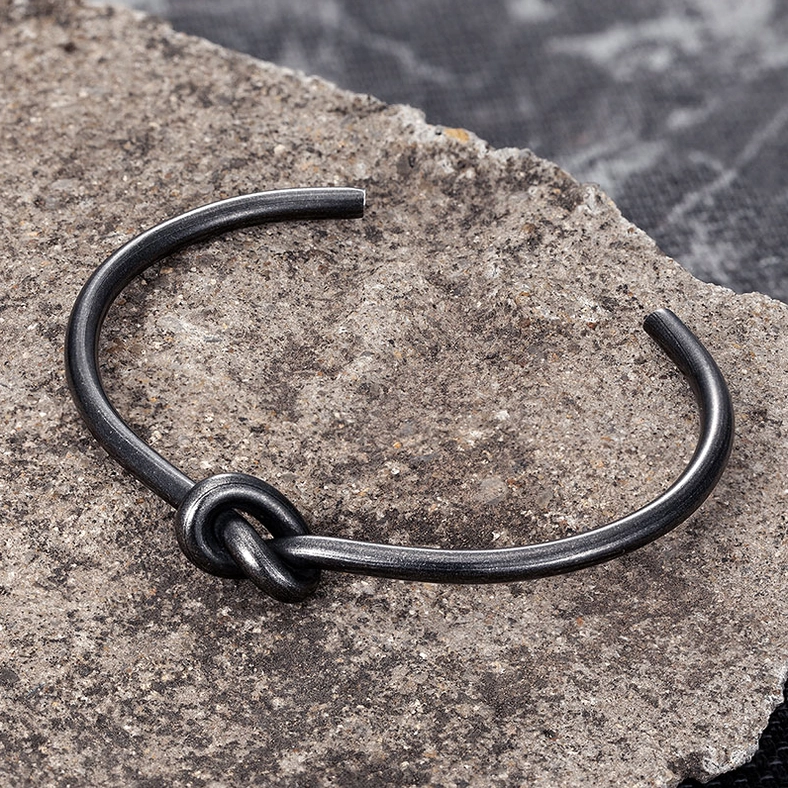 Matte black oxidized knotted open cuff gothic stainless steel bracelet detail shot on stone texture