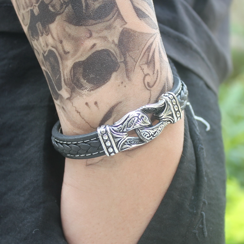 Close-up of genuine leather gothic bracelet worn on tattooed male forearm with dark clothing backdrop