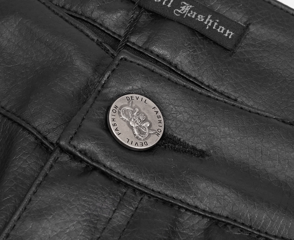Top-down close-up of black gothic leather pants fastener showing branded metal button and official clothing label tag