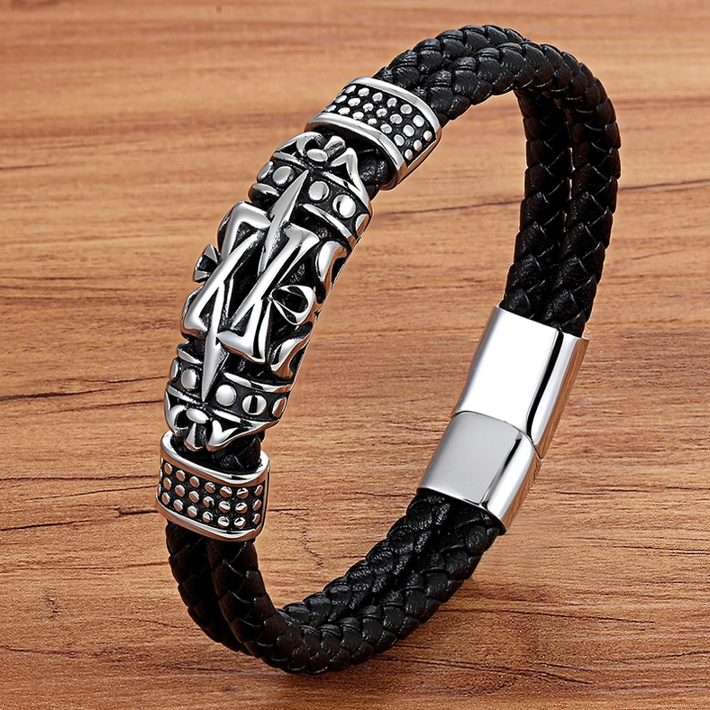 Black braided leather totem bracelet with silver metal ornament displayed on wooden surface, oblique angle showing bracelet construction and craftsmanship