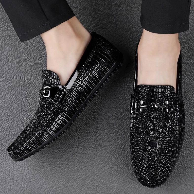 Two black gothic loafers with glossy crocodile-embossed leather, mixed front and side angle on gray textured surface