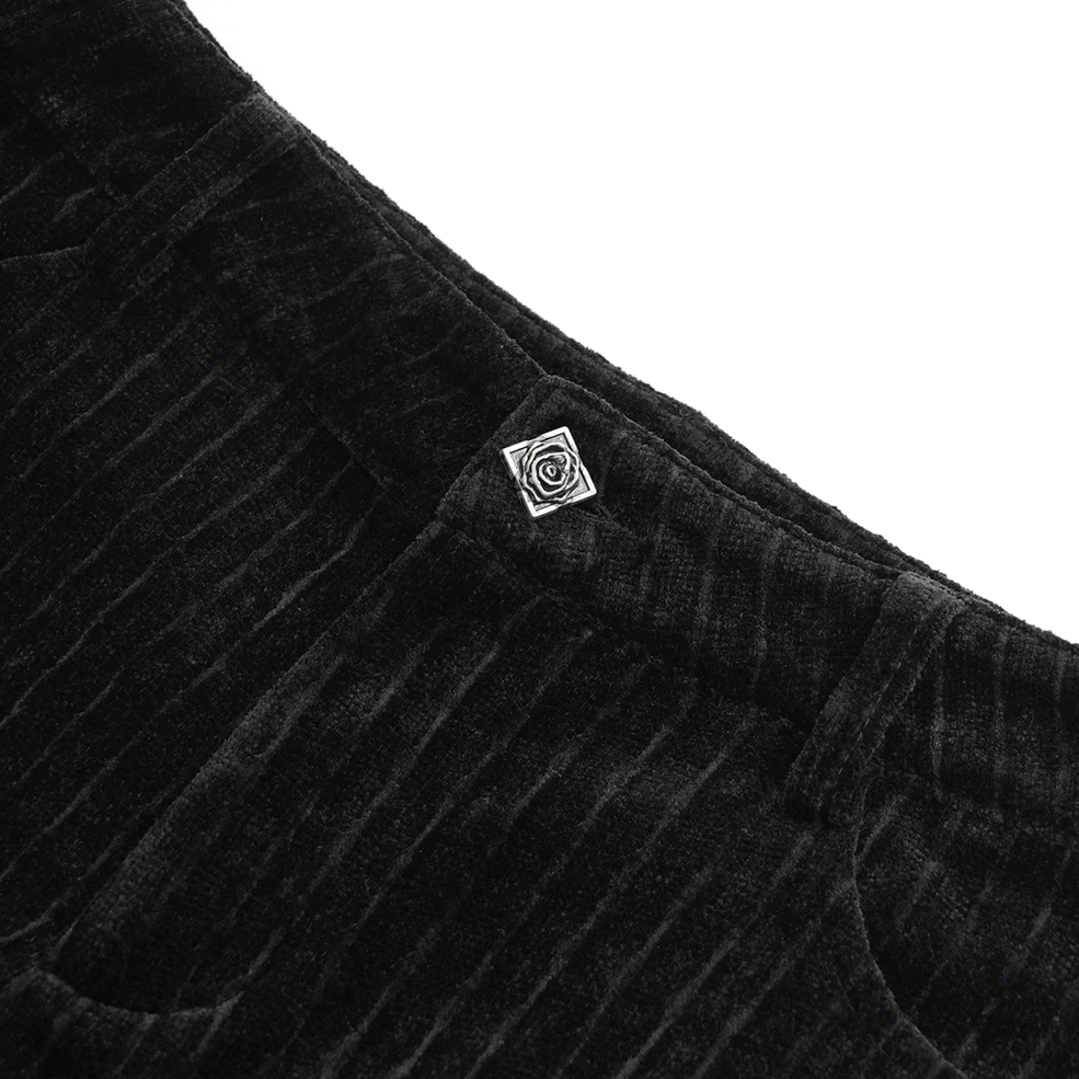 Black gothic pants waistband with rose-shaped metal badge and ribbed velvet texture - close up side view