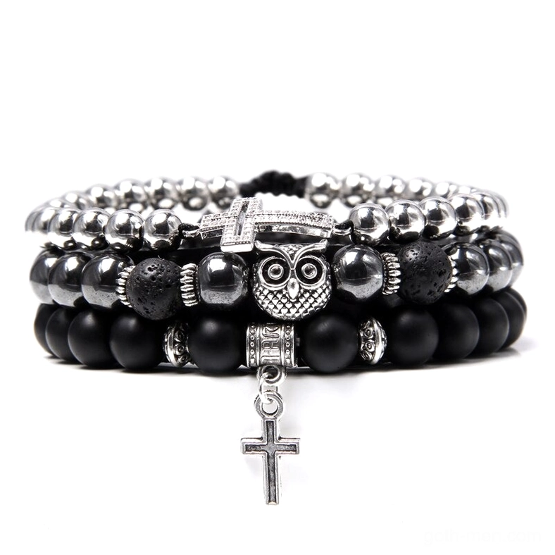 Silver gothic layered bracelet with black matte beads, owl charm, dangling cross pendant, and lava rock stones, flat lay photography