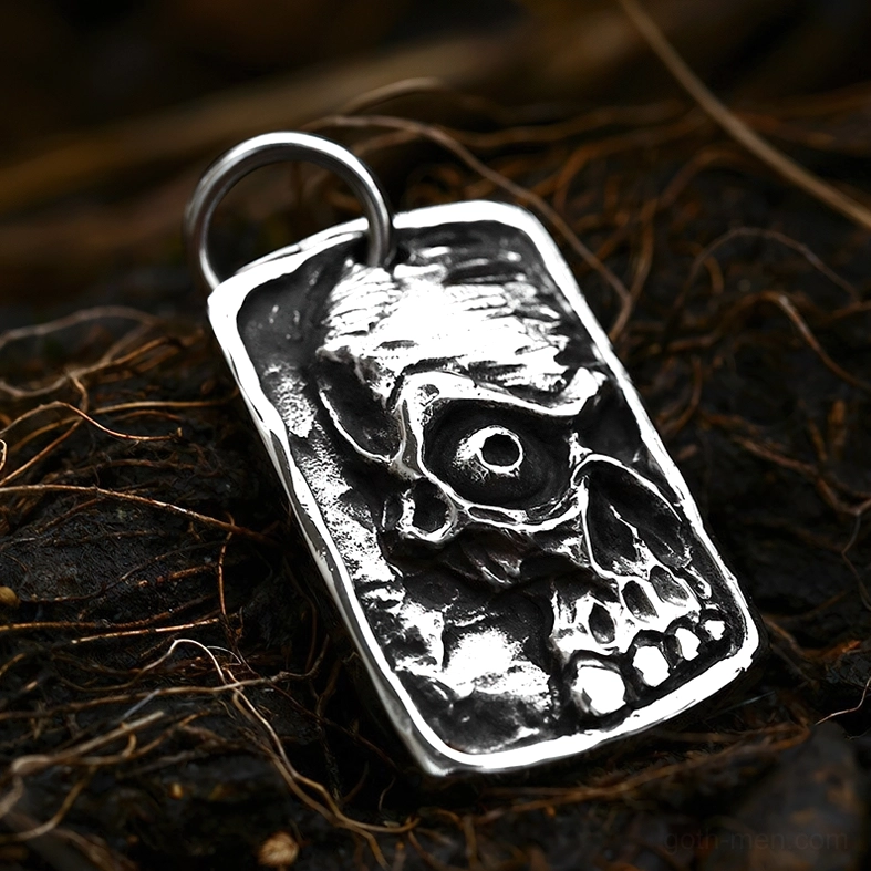 Vintage silver ghost skull dog tag pendant displayed on natural forest ground with gothic aesthetic styling