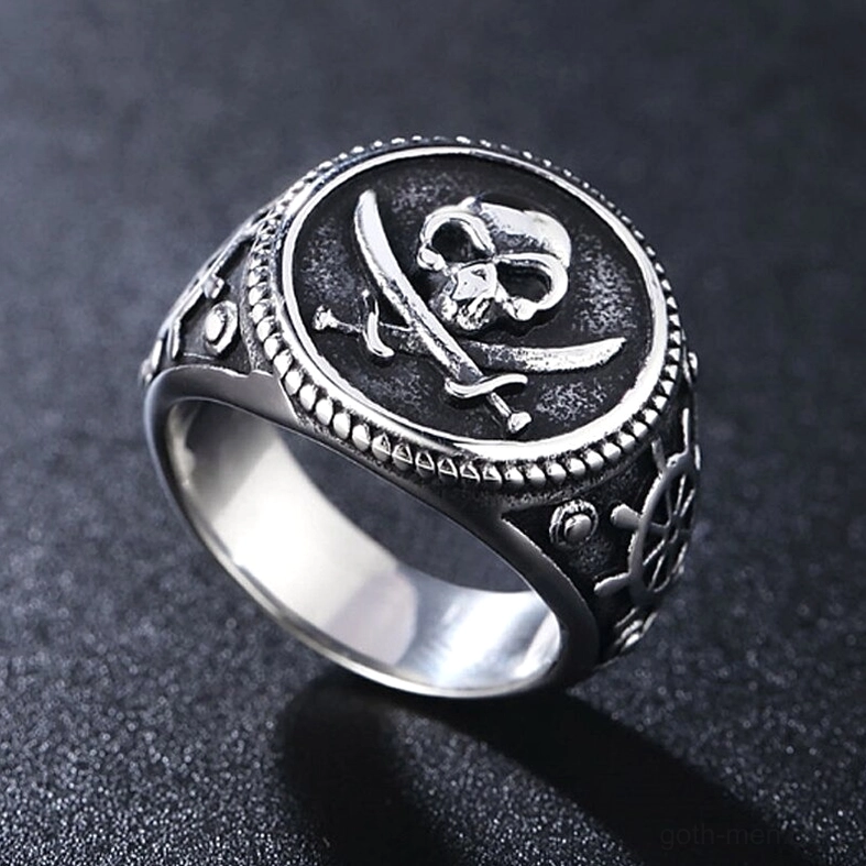 All-silver gothic skull pirate signet ring with ship wheel and braided border detail, three-quarter view on grey background