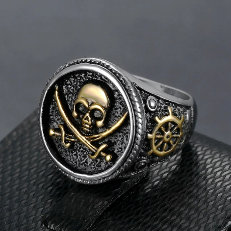 Two-tone gothic skull ring featuring gold crossed swords and ship wheel decoration on band, front three-quarter angle