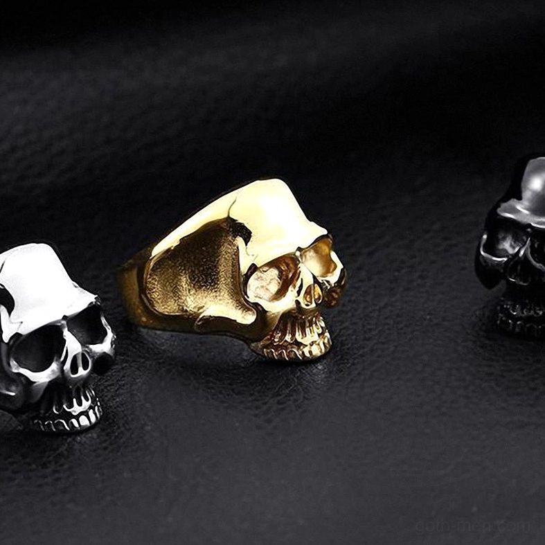 Three skull rings in black silver and gold options oblique view on smooth dark leather background showing complete gothic ring collection