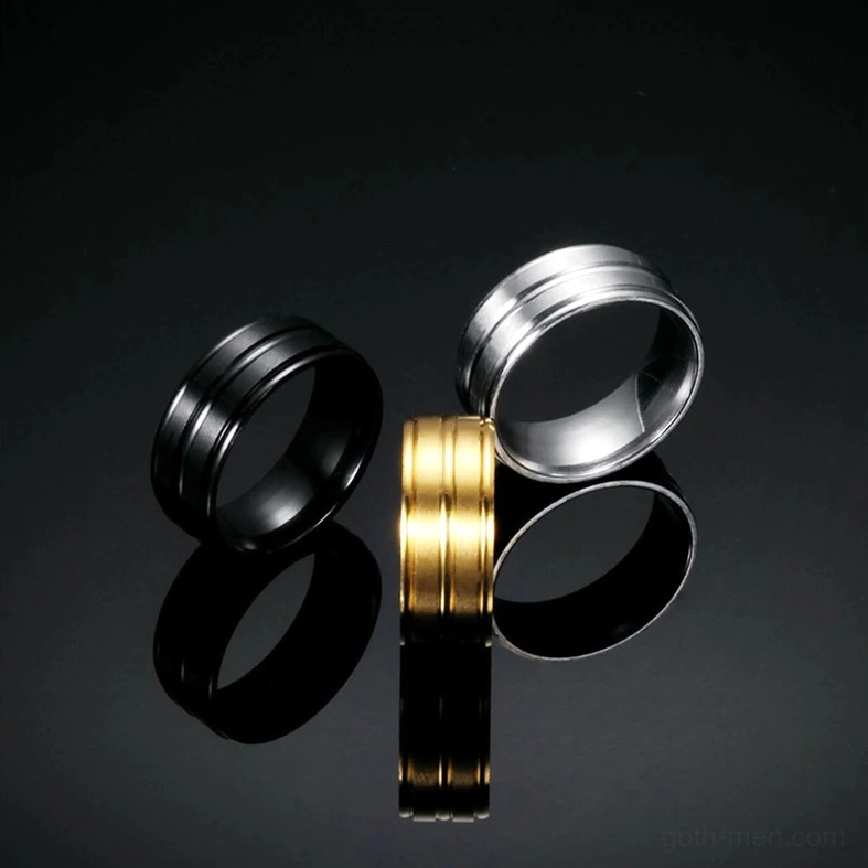 Triple gothic band rings in black, silver, and gold on mirrored black surface, flat product presentation