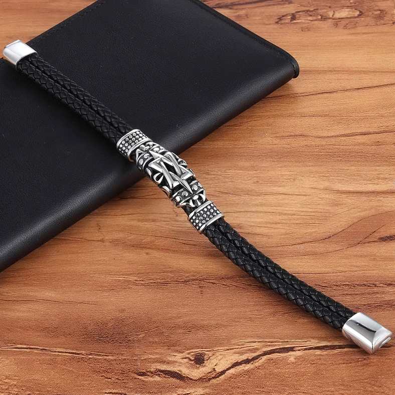Black leather totem bracelet lifestyle shot next to leather wallet on wooden surface, oblique angle highlighting vintage carved totem design and magnetic buckle
