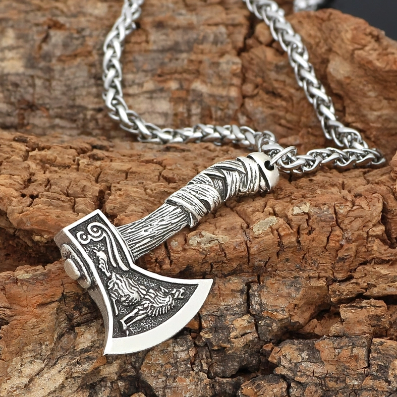 Antique silver gothic Viking axe necklace with wolf carving and wheat link chain, flat overhead perspective on textured bark