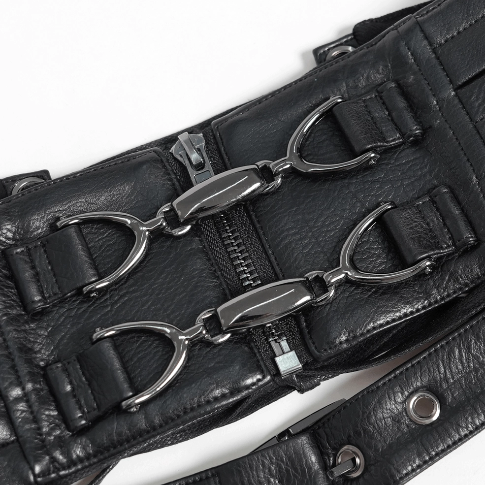 Close-up flat lay detail shot of black harness hardware, metal D-rings, zippered pockets, rivets, and leather construction details