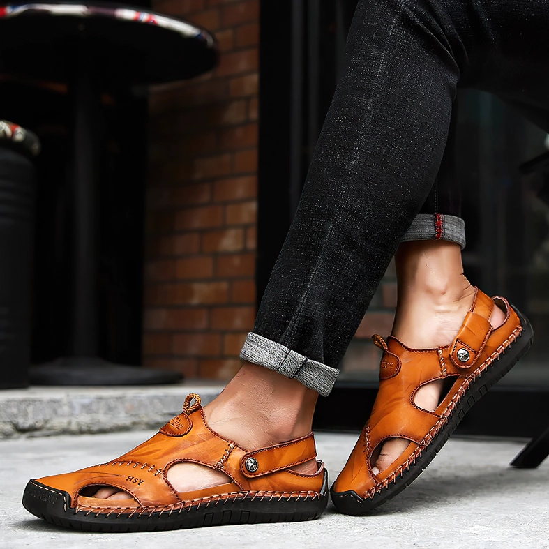 Man styled in rolled-up denim wearing light tan leather gothic sandals with hand-stitched closure on pavement