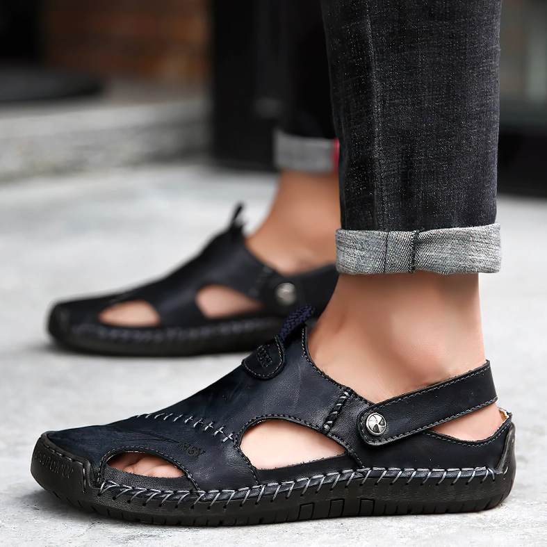 Male model wearing black leather gothic buckle sandals with both feet visible on pavement, outdoor lifestyle