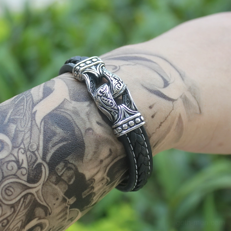 Tattooed man wearing gothic leather bracelet on wrist outdoors with green foliage background
