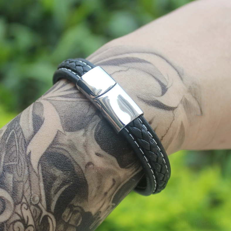 Plain leather variant of men's gothic bracelet worn on tattooed wrist with green outdoor background