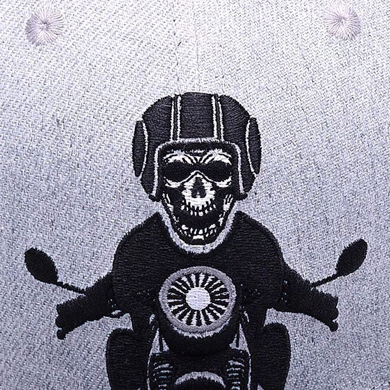 Macro close-up of intricate black thread embroidery depicting helmeted skeleton riding motorcycle on gothic cap