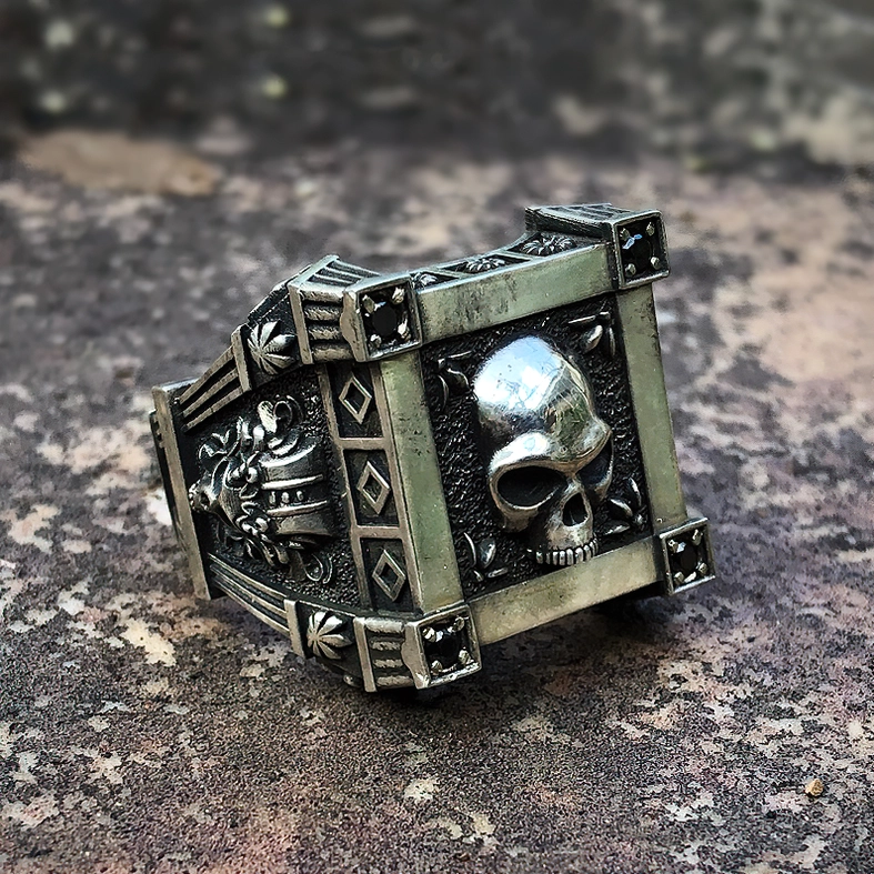 Biker skull ring three-quarter side view showcasing ornate relief carvings, geometric frame, and intricate metalwork