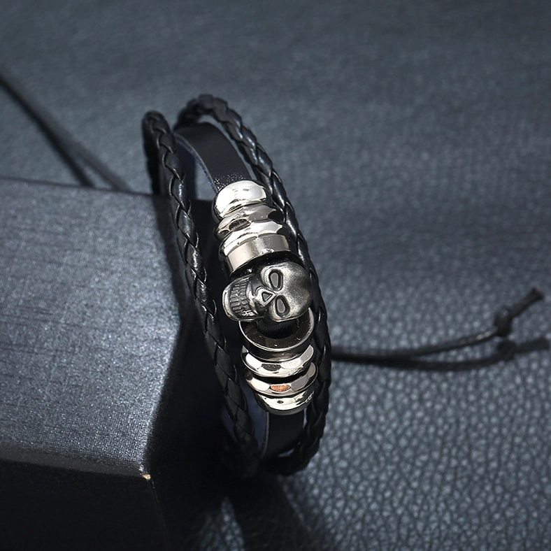 Close-up detail shot of gothic skull bracelet centerpiece showing silver-toned skull charm, stacked metal discs, and intricate braided leather edges