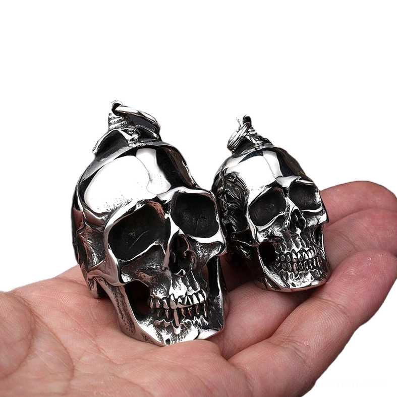 Dual-size stainless steel skull pendants displayed on palm with white background showing size comparison