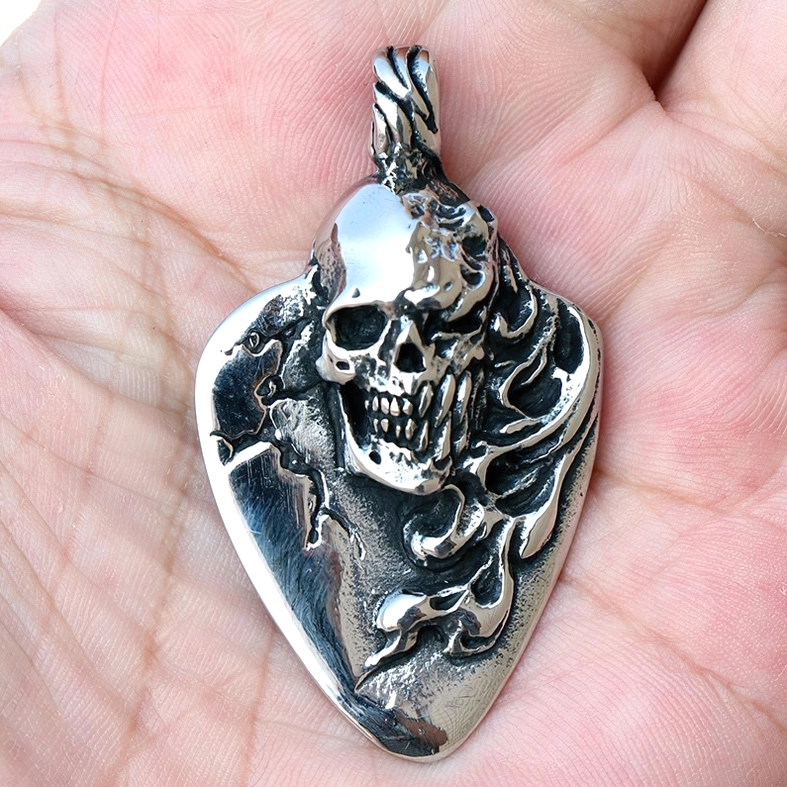3D carved skull guitar pick pendant held in palm, overhead angle showcasing antique finish details